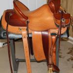 Trainer -2 tone, 2 strand barbed wr w channels, corner basket wv, latigo wrap, stirrup lthrs out, 2 in bell stirrups, straight-back, matching pouch, floral conchos