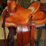 Trainer - barbed wire w channels border, stirrup lthrs out, star conchos, latigo wrap, hand-carved elk horns on front, straight-back